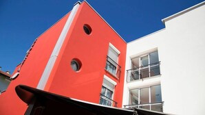 Un bâtiment moderne à la façade rouge et à la partie blanche, doté de balcons et de grandes fenêtres.