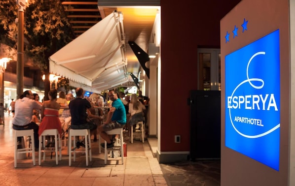 An outdoor seating area with white tables and chairs, a white canopy, and a sign for "Esperya Apart Hotel". - Aparthotel Esperya (Lignano Sabbiadoro)