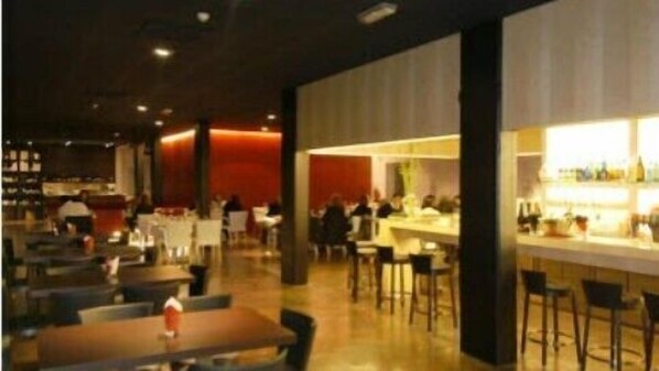 A modern restaurant with a bar area, multiple tables, and a warm ambient lighting. - Aparthotel Esperya (Lignano Sabbiadoro)