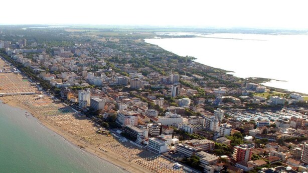 Vue aérienne d’une ville côtière avec une longue plage, une zone urbaine densément peuplée et une jetée dotée de diverses constructions.