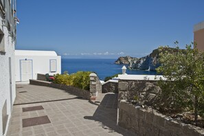 A coastal building with a paved pathway leading to a white door, overlooking the sea.