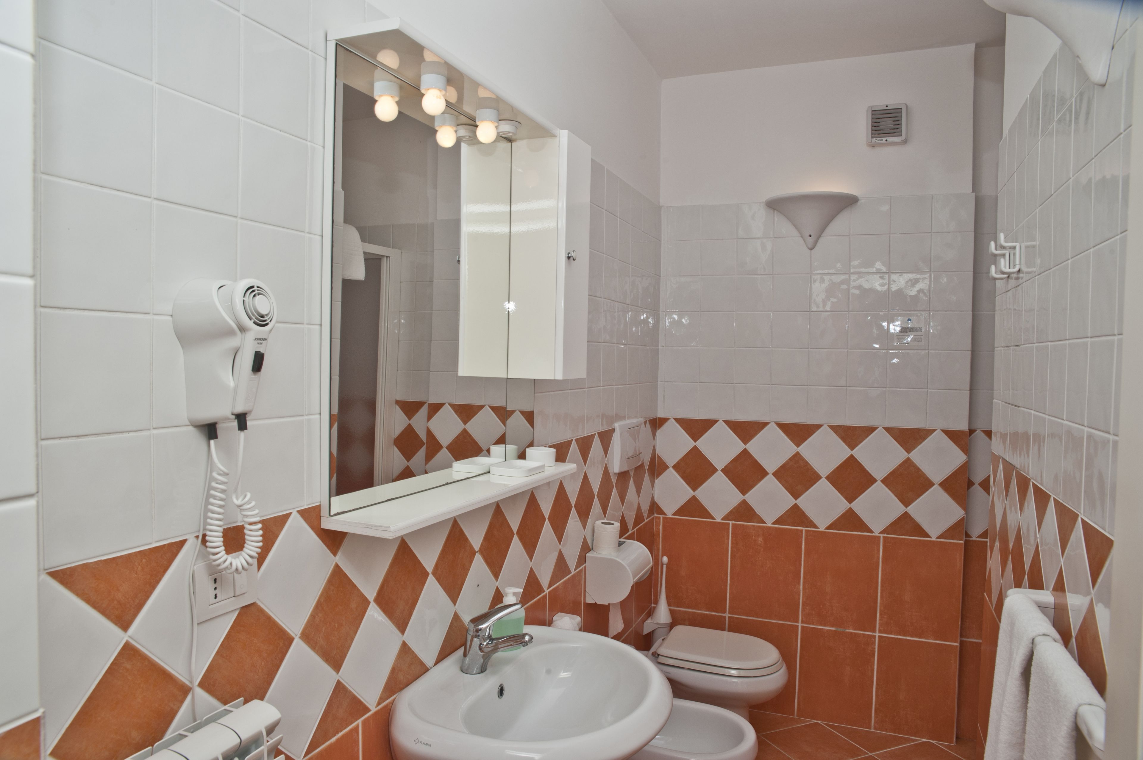 Un baño con lavamanos, inodoro y un secador de pelo en la pared.