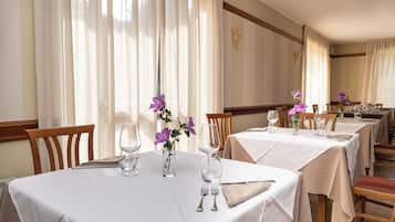 A restaurant with tables set for dining, featuring white tablecloths and purple flowers.