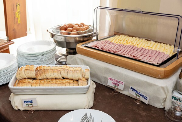 A buffet with labeled food items including bread, ham, cheese, and eggs. - Hotel Valentino (Acqui Terme)