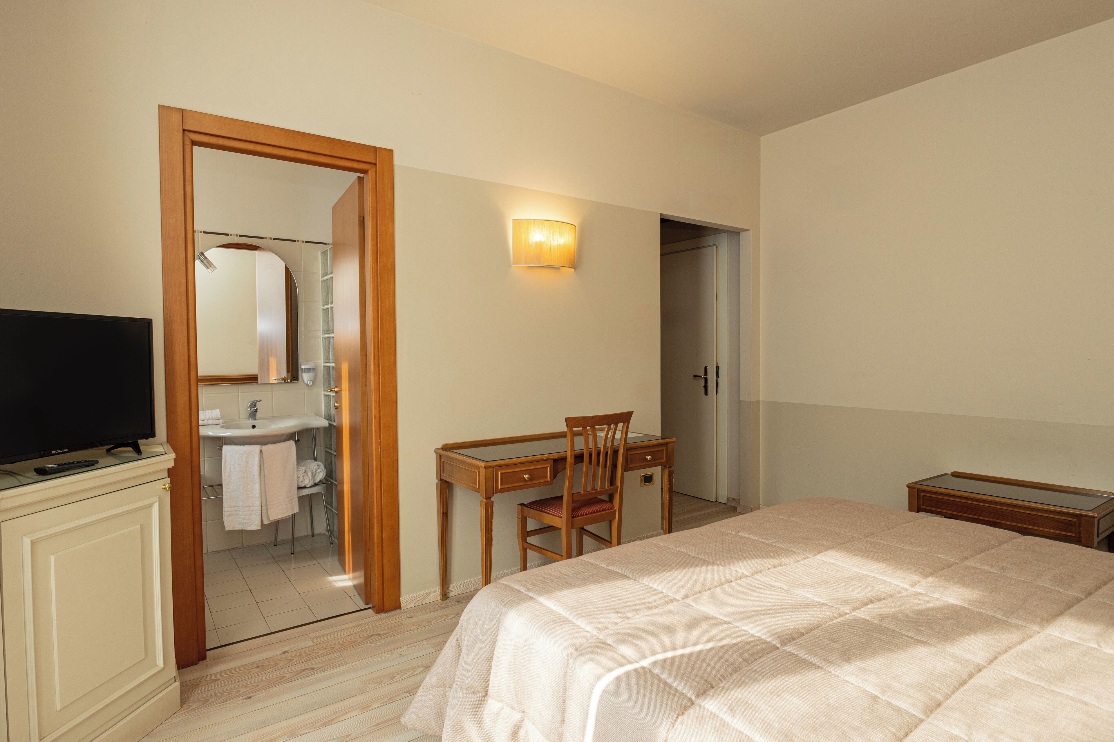 A hotel room with a bed, a desk, a chair, a television, and a bathroom visible through an open door.