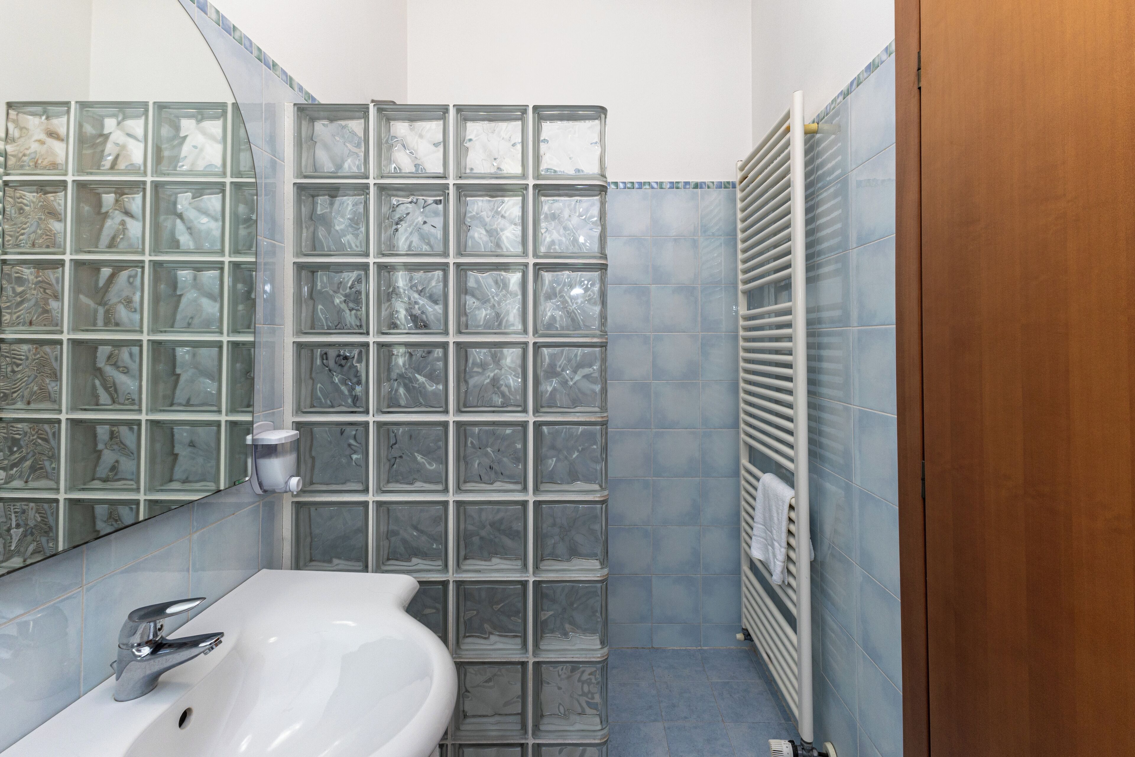 A bathroom with a white sink, a mirror, and a tiled shower enclosure.