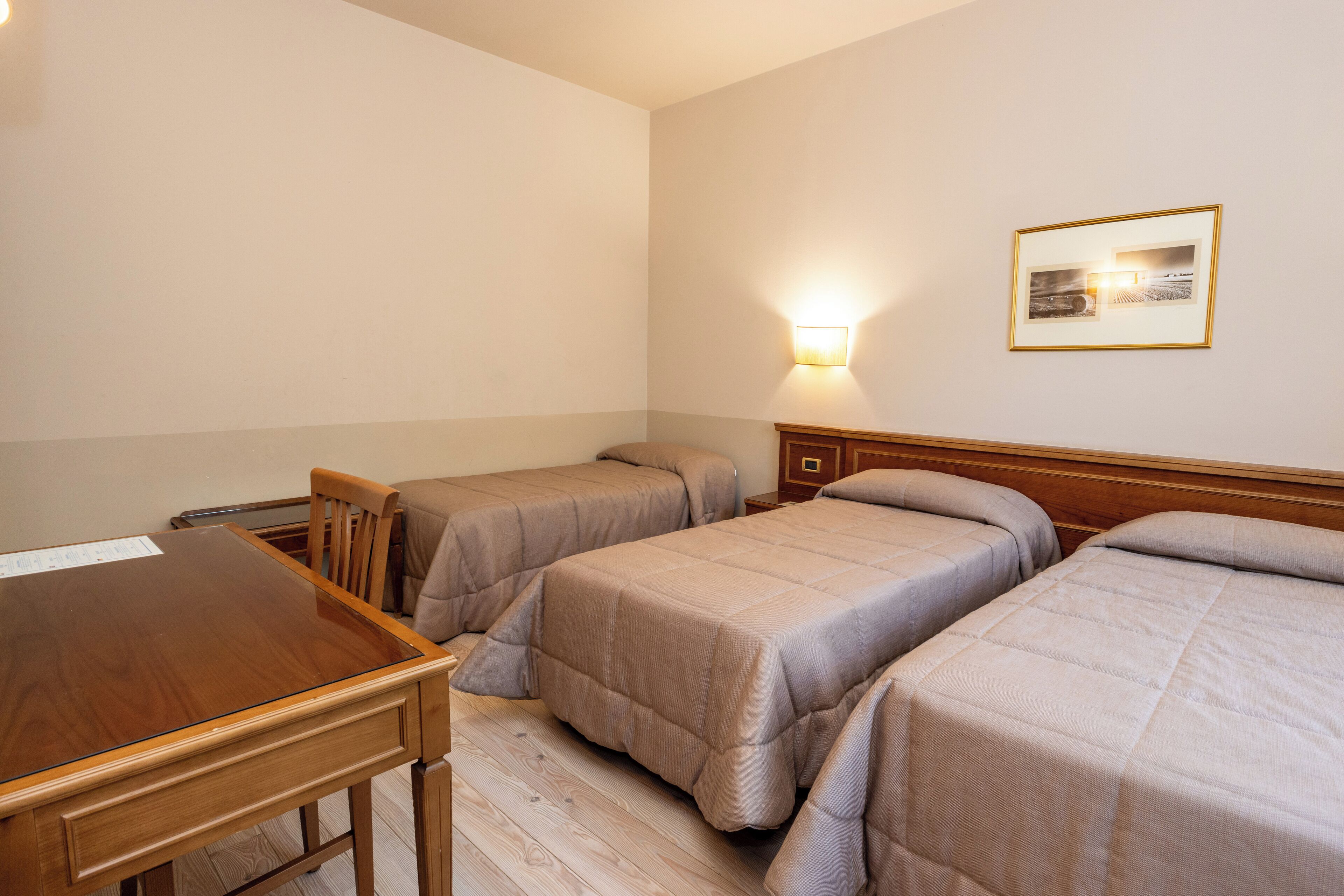 Ein Hotelzimmer mit Holztisch, zwei Einzelbetten, einem Nachttisch aus Holz, einer Wandlampe und einem gerahmten Bild.
