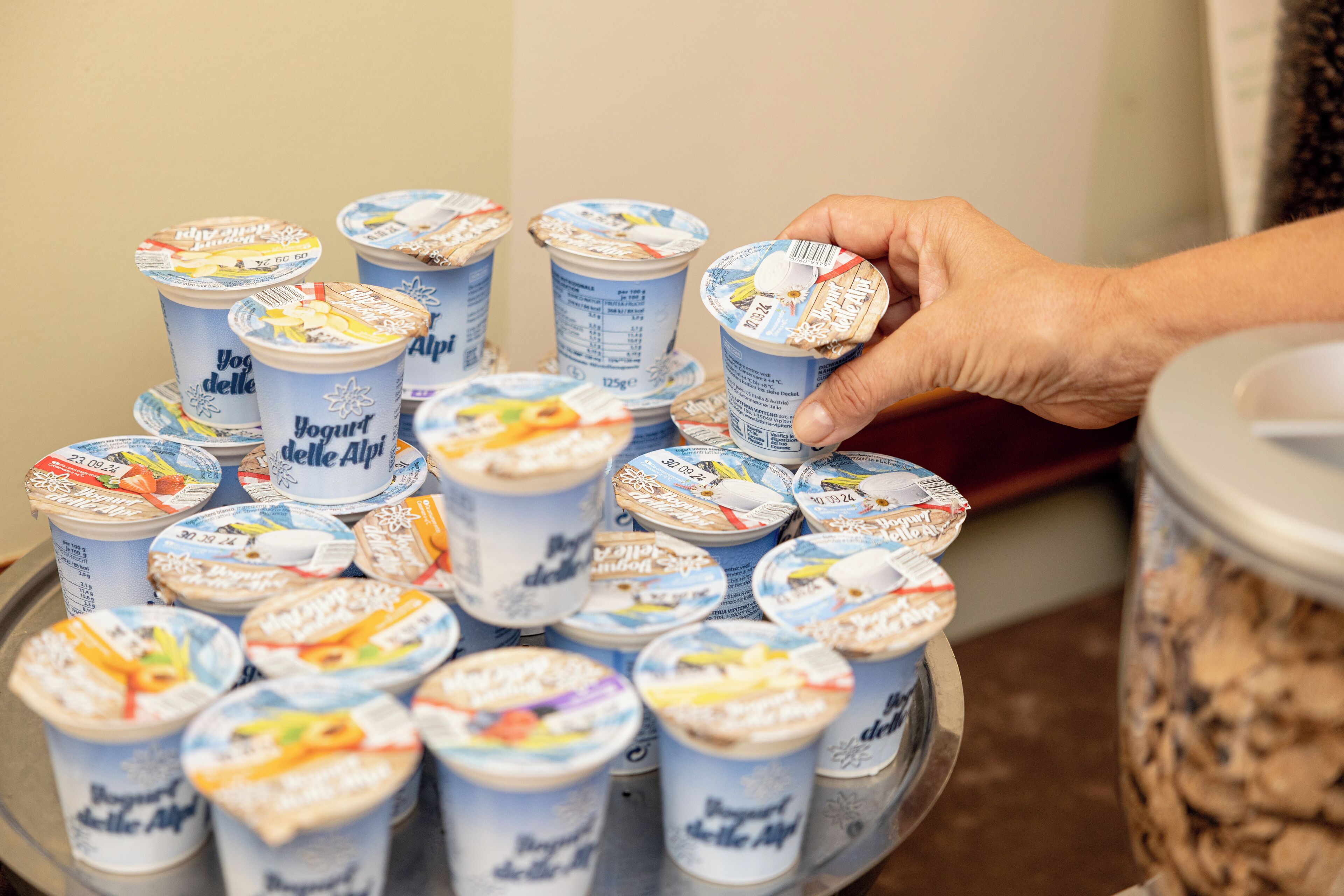 A hand reaching for a yogurt container on a metal tray.