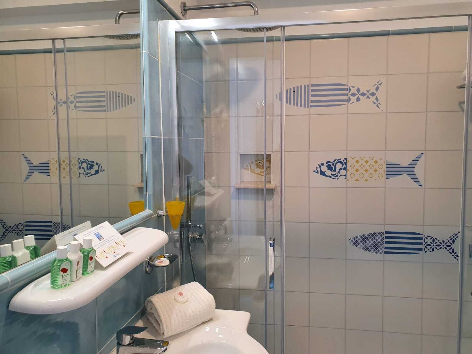 Un baño con cabina de ducha de vidrio, lavamanos con artículos de aseo y azulejos decorativos con motivos de peces.