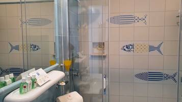 Un baño con cabina de ducha de vidrio, lavamanos con artículos de aseo y azulejos decorativos con motivos de peces.