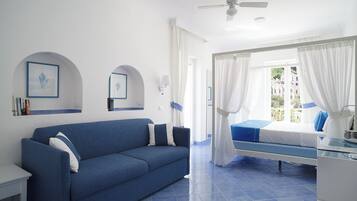 A room with a blue sofa, a bed with a canopy, a ceiling fan, and a view of buildings through the window.