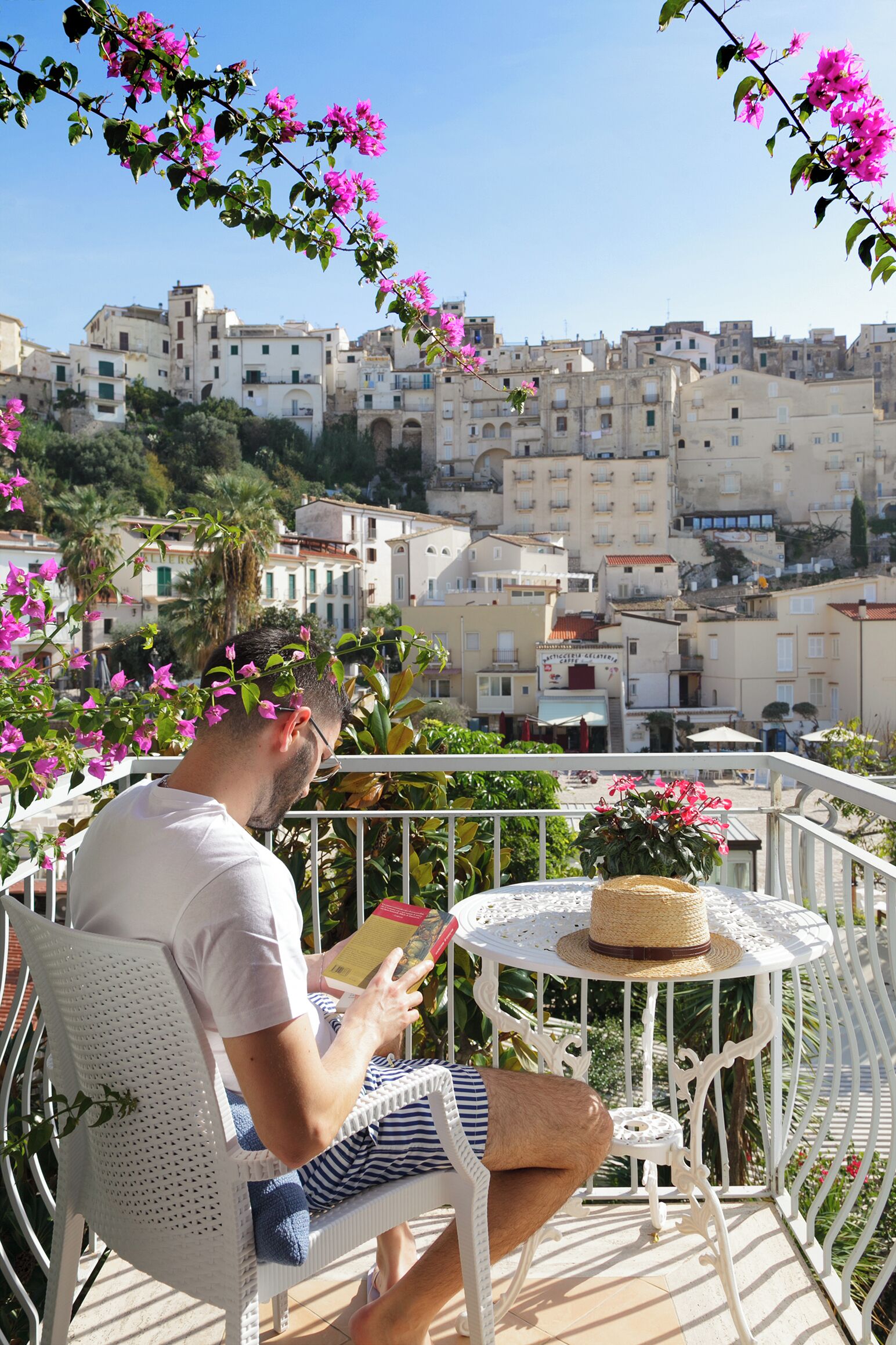 A man reading a book on a balcony with a view of a cityscape.