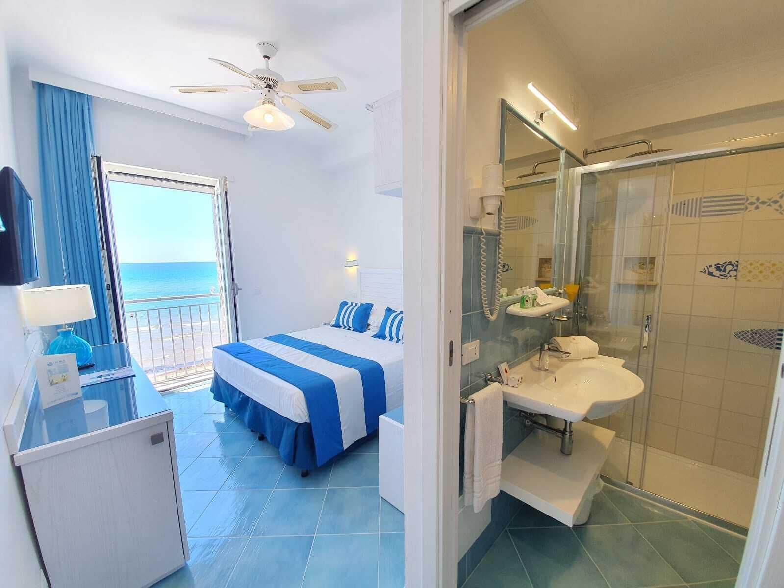 Ein Hotelzimmer mit Bett, einem Badezimmer mit Duschkabine und einem Balkon mit Meerblick.