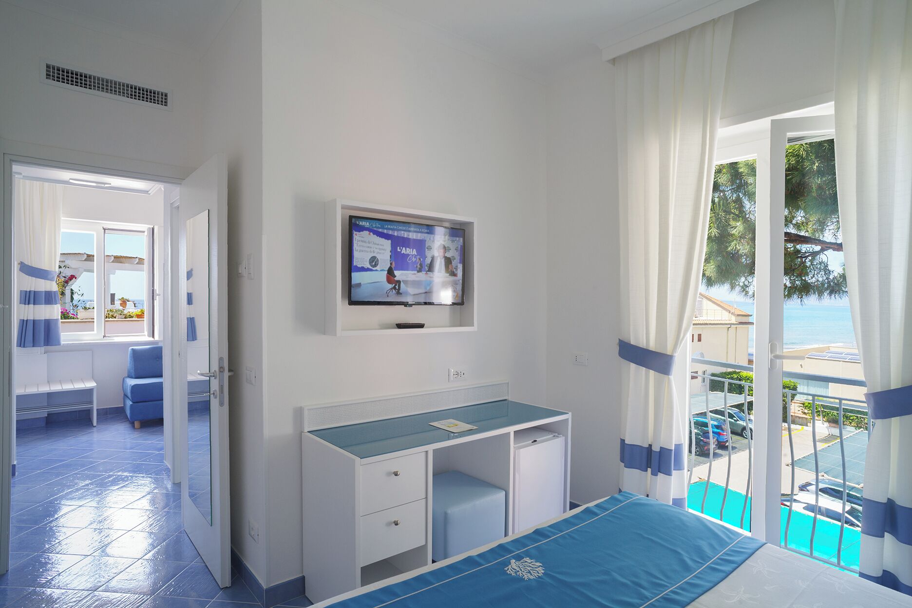A hotel room with a bed, a desk, a TV, and a balcony with a pool view.