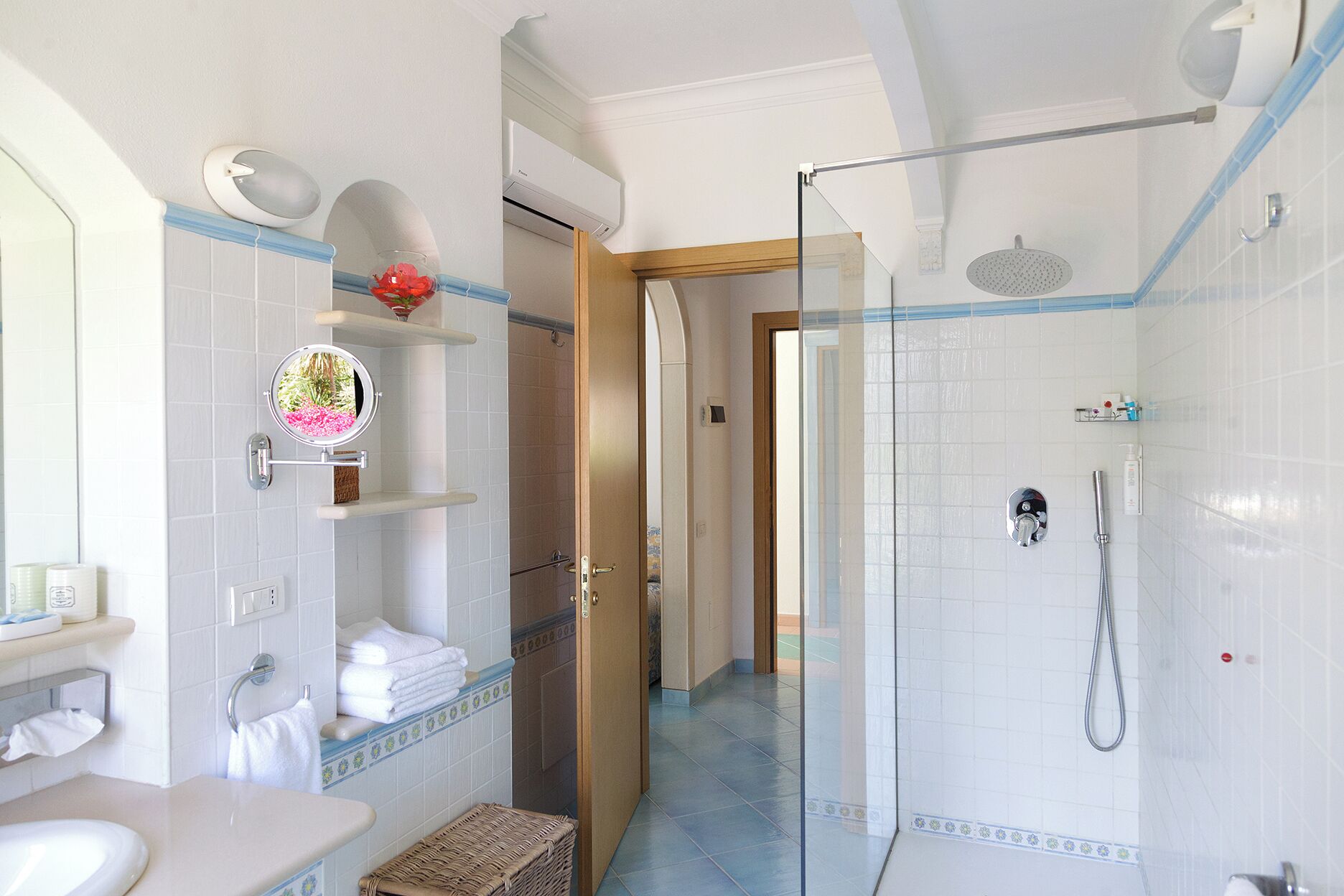 A modern bathroom with a glass-enclosed shower, white tiled walls, and a visible door leading to another room.