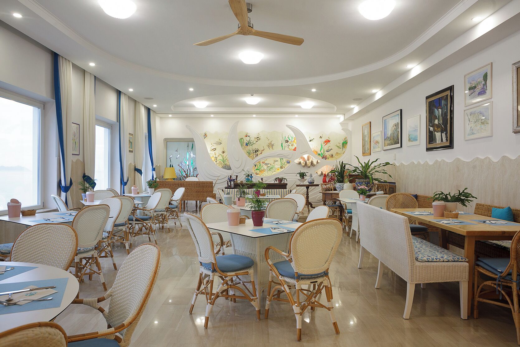 A spacious dining area with wicker furniture, ceiling fans, and wall art.