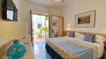 A hotel room with a bed, a desk with a lamp, a ceiling fan, and a view of the outdoor patio.