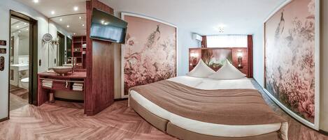 A modern bedroom with a large bed, a TV, and a bathroom with a vanity and sink.