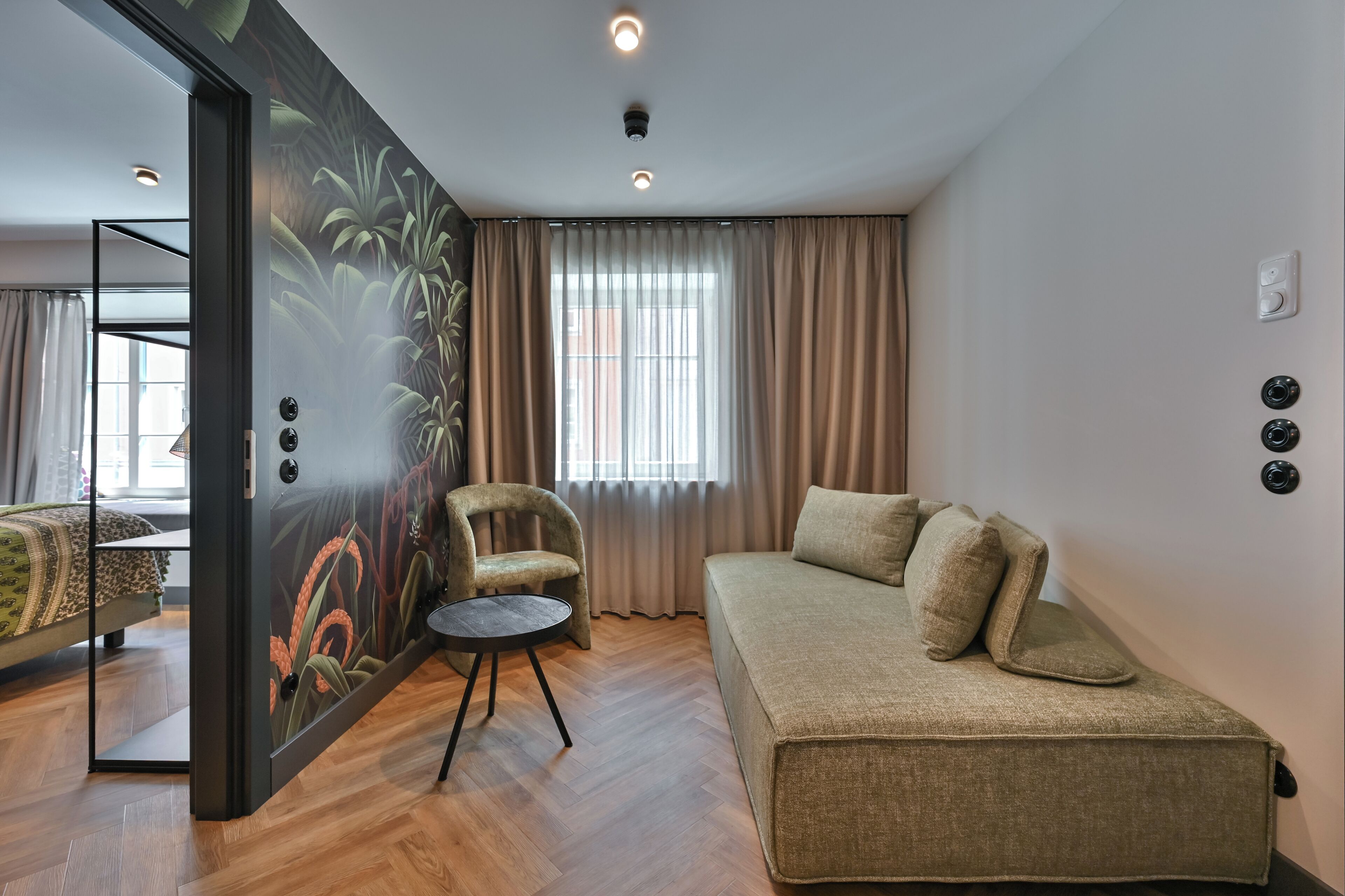Ein modernes Zimmer mit einer Couch, einem Sessel, einem kleinen Tisch und einem großen Fenster mit Vorhängen.