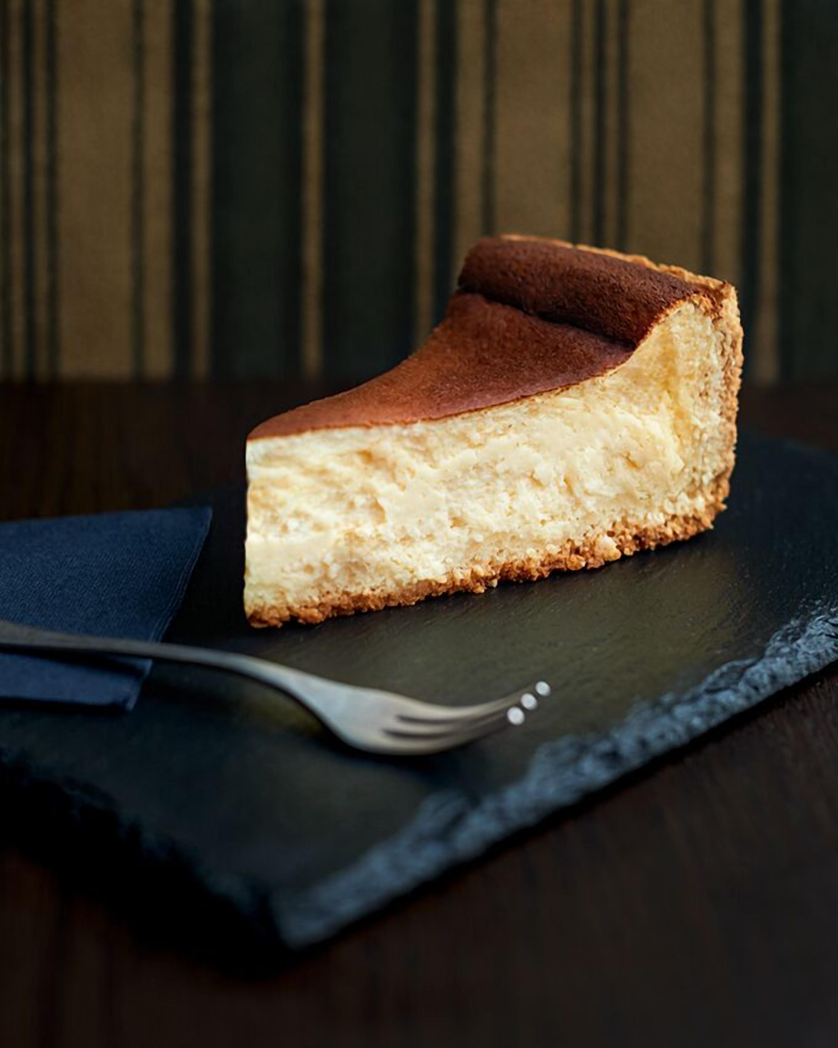 A slice of cheesecake on a dark slate plate with a fork beside it.