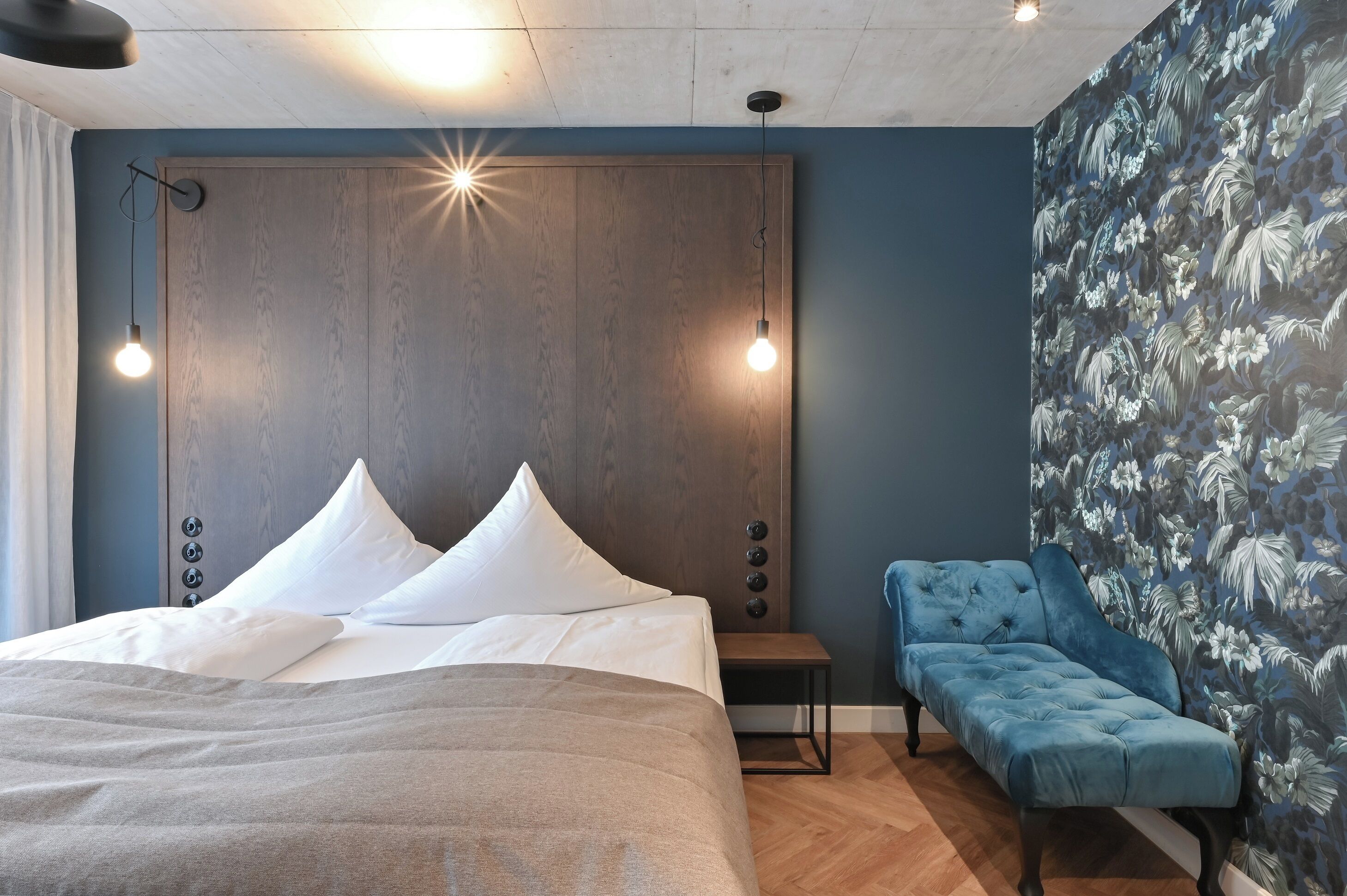 Un dormitorio con una cama grande, dos lámparas de noche, una mesita pequeña y un sofá azul.