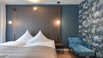 Un dormitorio con una cama grande, dos lámparas de noche, una mesita pequeña y un sofá azul.