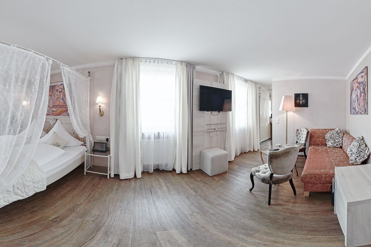 Habitación de hotel con cama con dosel, televisor de pantalla plana, sofá y escritorio.