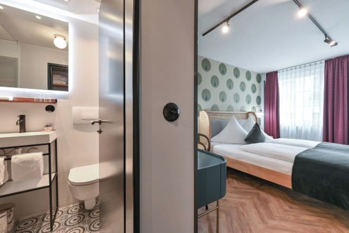 Habitación de hotel moderna con cama, mesita de noche, espejo, inodoro y zona de ducha.