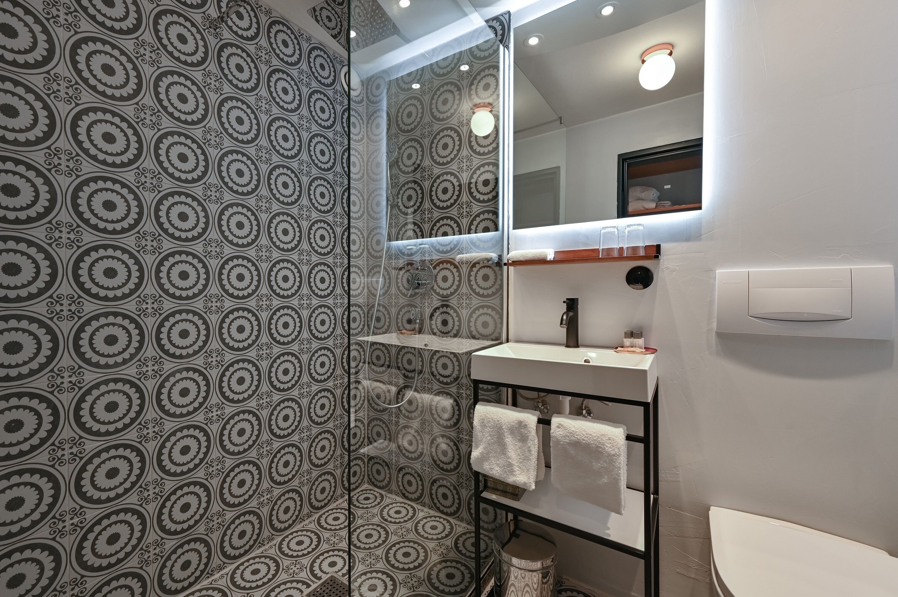 A bathroom with patterned wallpaper, a mirror, a sink, and a toilet.