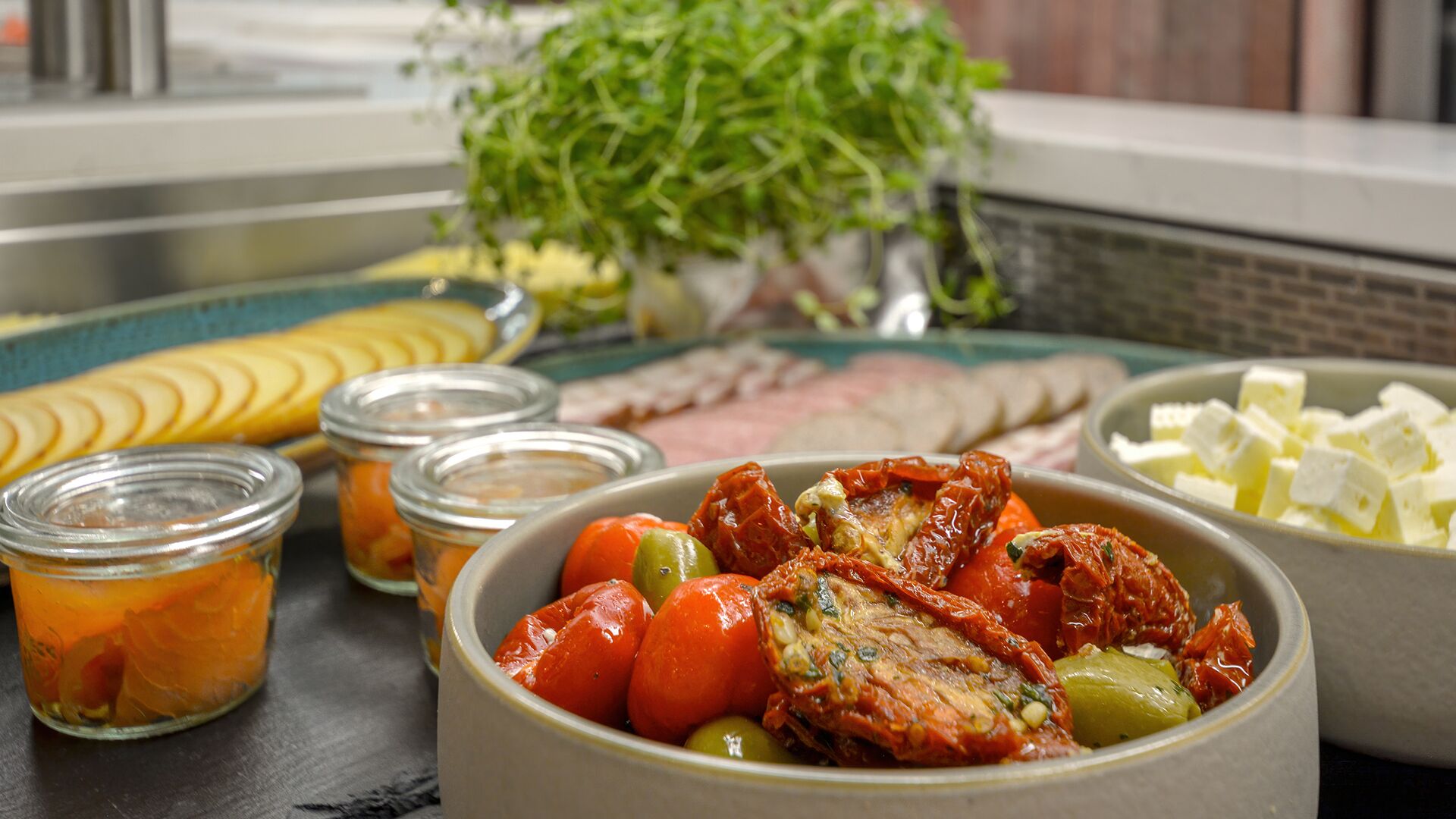 A variety of food items including sliced apples, tomatoes, olives, and a bowl of cheese.
