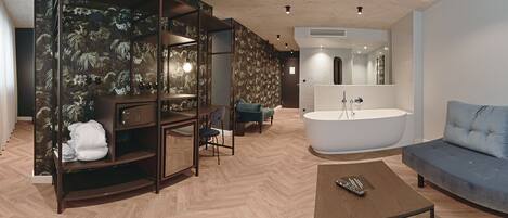 A modern bathroom with a freestanding bathtub, a vanity with a mirror, and a seating area with a blue sofa and armchair.