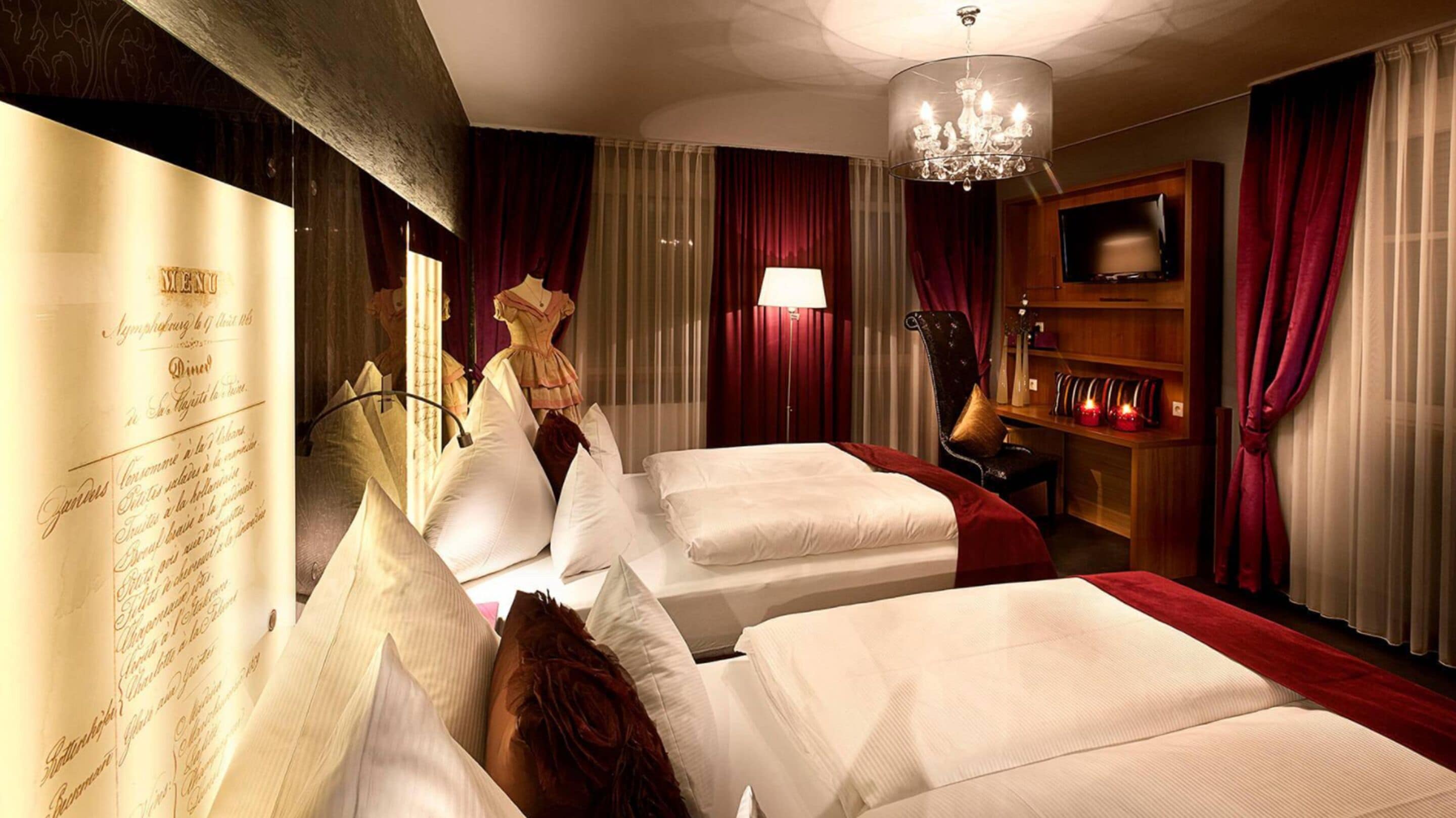 A hotel room with two beds, a chandelier, a television, and a minibar.