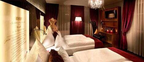 A hotel room with two beds, a chandelier, a television, and a minibar.