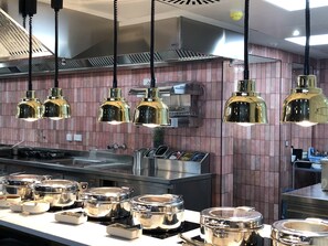 Cocina comercial con electrodomésticos de acero inoxidable, luces colgantes y salpicadero de azulejos.