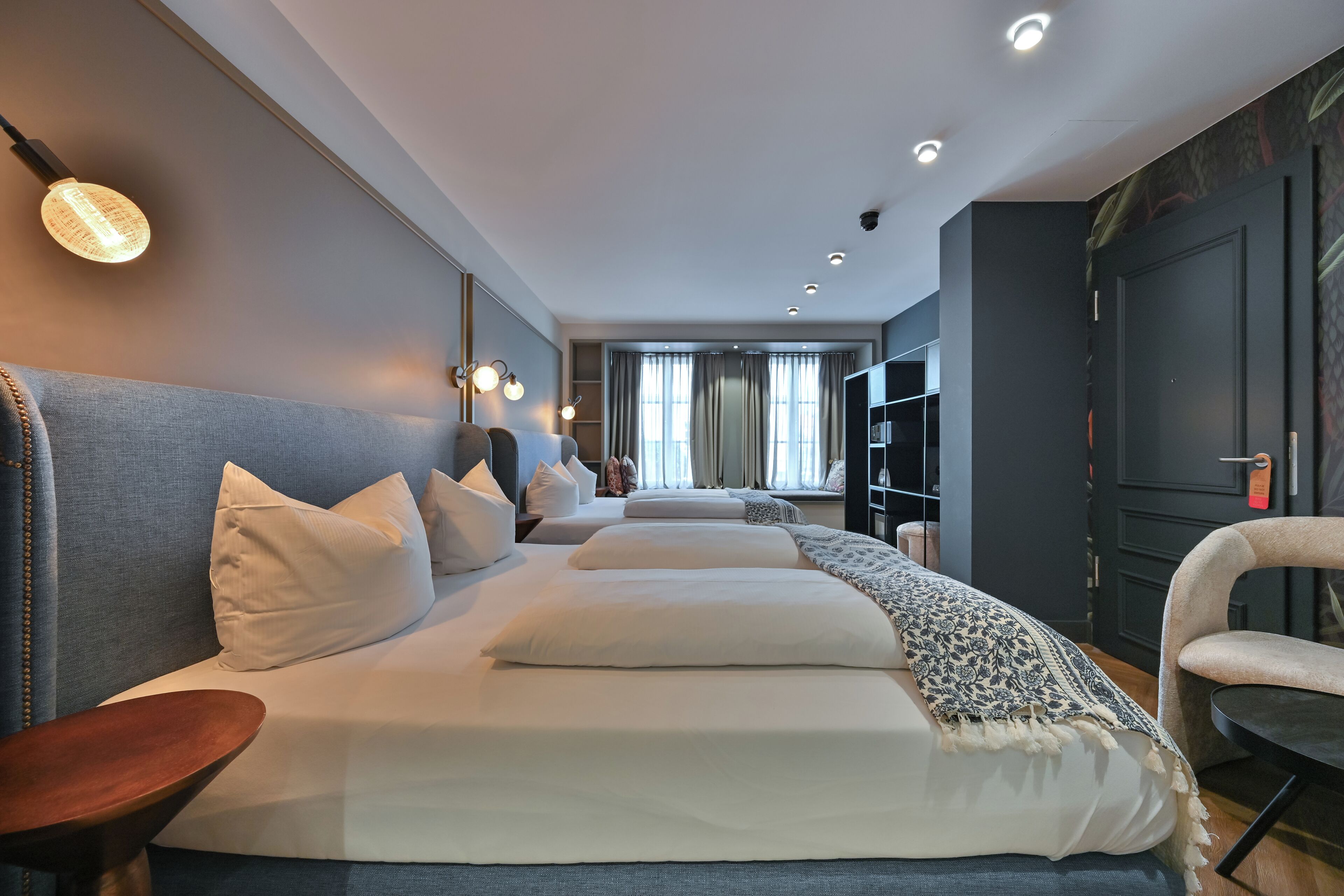 Une chambre d’hôtel moderne avec un grand lit, une table de chevet en bois et un coin salon avec un fauteuil.