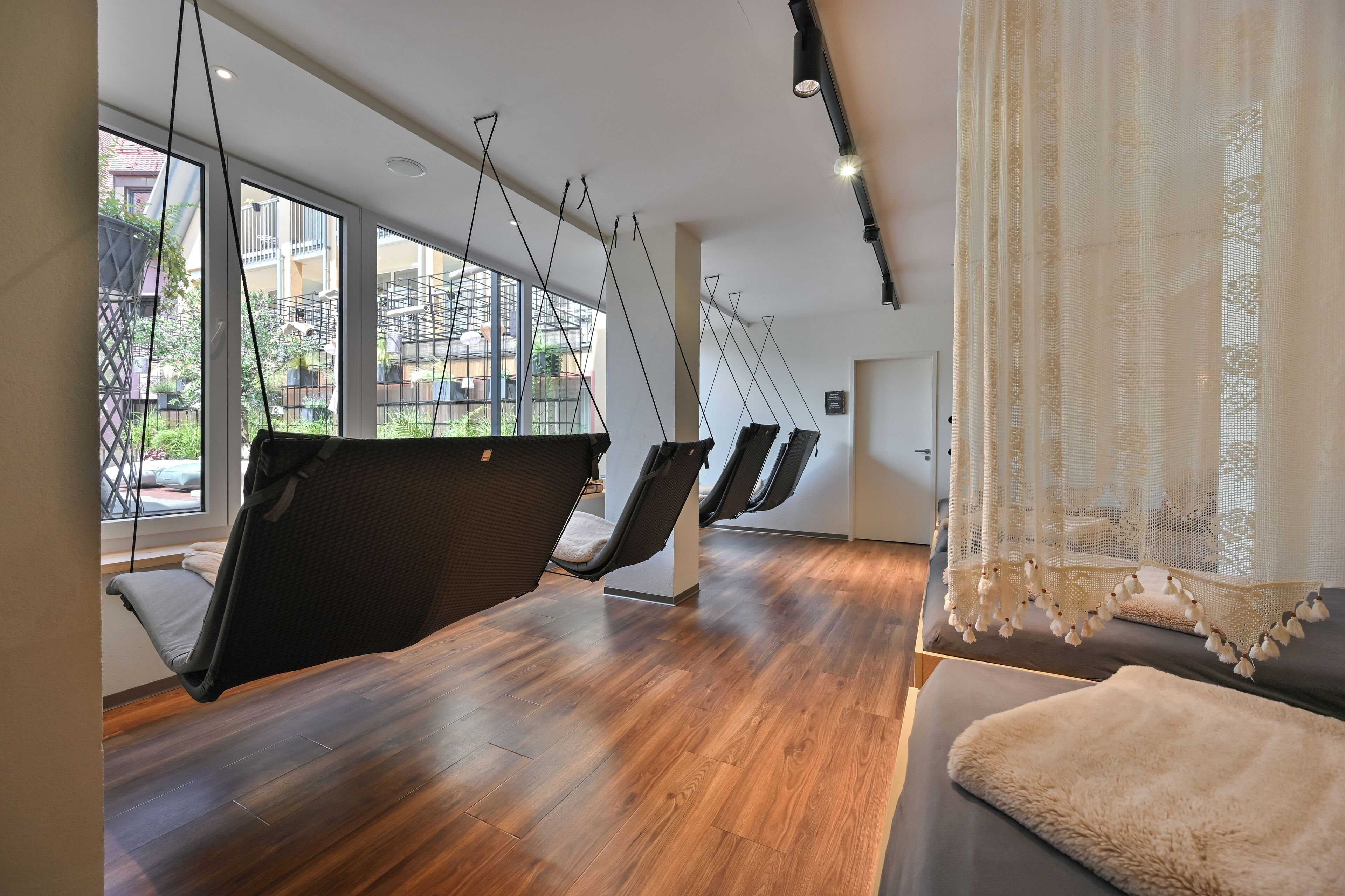 Una habitación con suelo de madera, un sofá y un sillón colgante con cojín negro.
