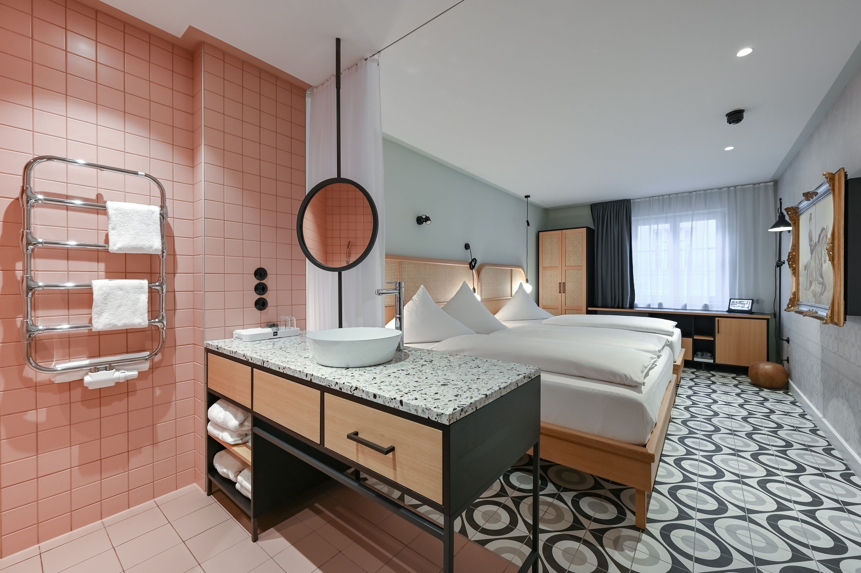 A modern hotel room with a bed, a bathroom with a sink and towel rack, and a patterned floor.