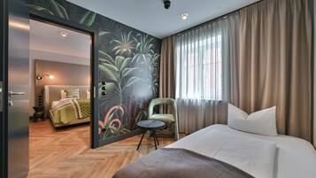 Habitación de hotel con cama, una silla, un espejo y un mural temático tropical.