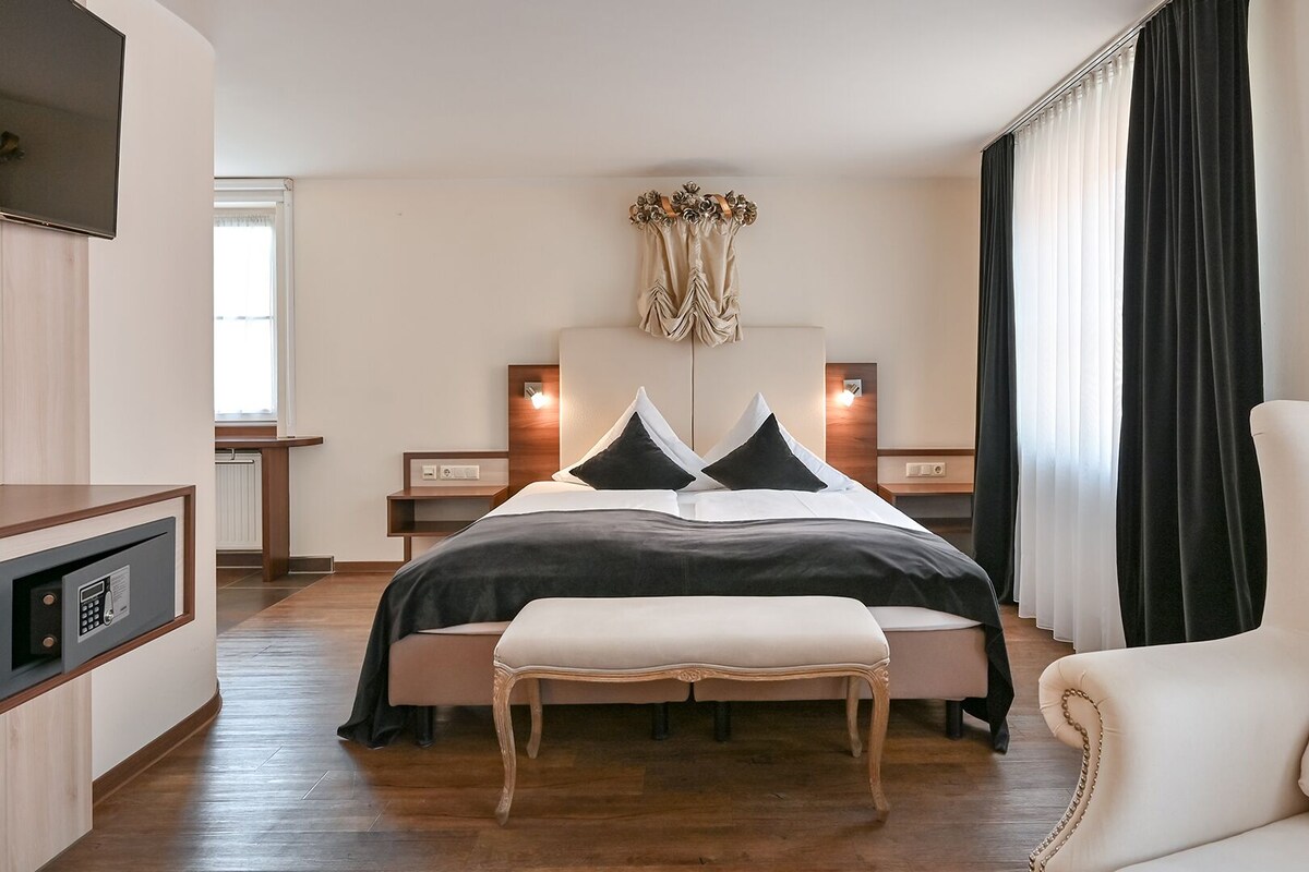 Una habitación de hotel moderna con una cama grande, una mesita de noche, una silla, un televisor y una caja fuerte.