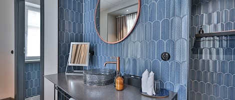 Un baño con encimera gris, un espejo redondo, un lavabo con grifo de cobre y una pared con diseño.