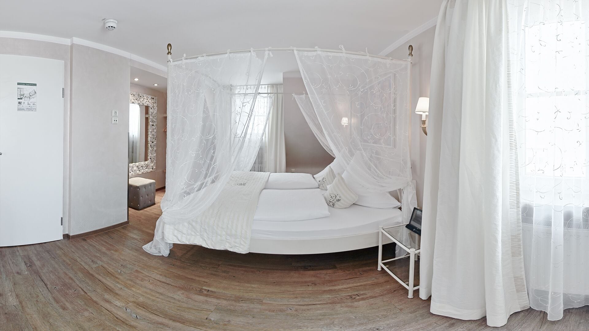 Ein Schlafzimmer mit einem Himmelsbett, einem runden Holzboden, einem Nachttisch und einer Lampe.