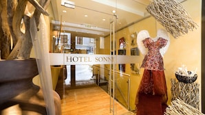 Entrada de hotel con puerta de cristal, suelo de madera y un vestido en exhibición.