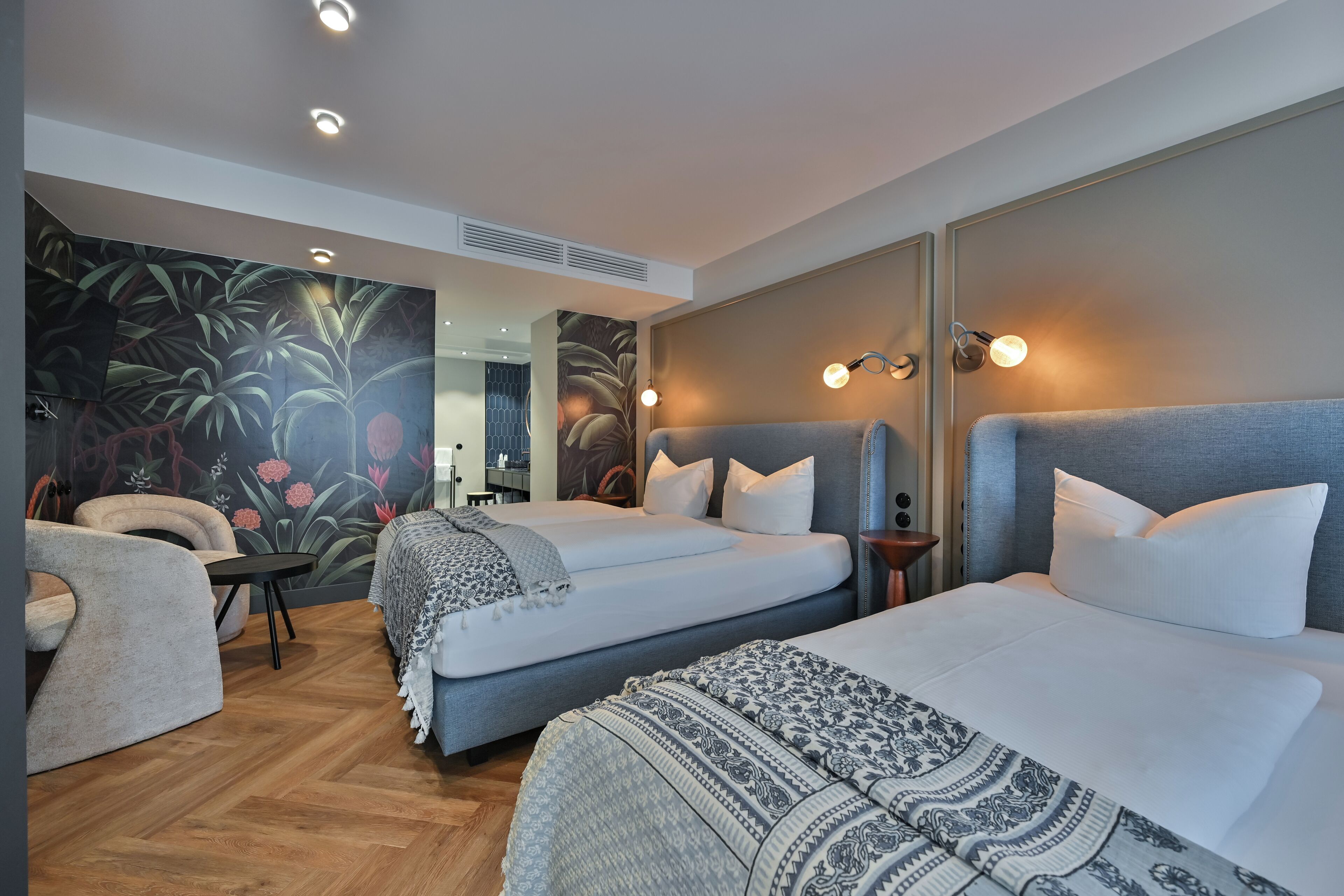 A modern hotel room with two beds, a sofa, a small table, and a mural on the wall.