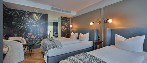 A modern hotel room with two beds, a sofa, a small table, and a mural on the wall.