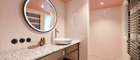 Un baño moderno con un lavamanos blanco, un espejo redondo y un calentador de toallas.
