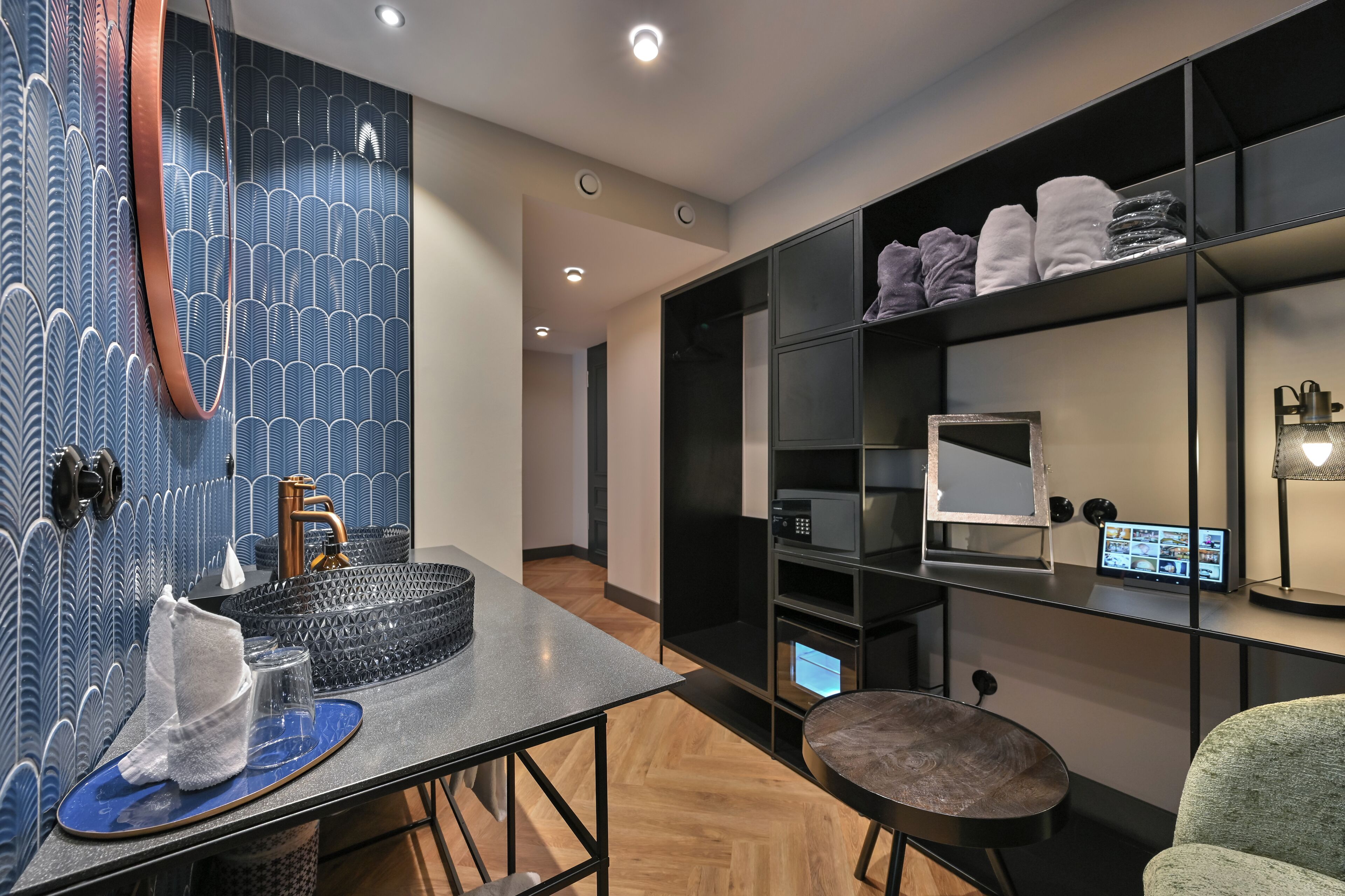 Une salle de bain moderne avec un mur à motifs bleus, un lavabo avec un robinet en cuivre, un miroir et une étagère avec des serviettes.