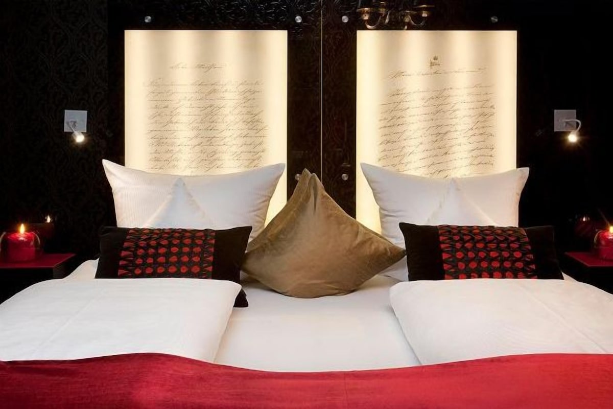 Una habitación de hotel con una cama grande, dos mesitas de noche y una pared con inscripción iluminada.