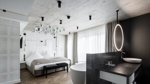 Un dormitorio moderno con una cama grande, un banco, una bañera y un tocador con espejo.