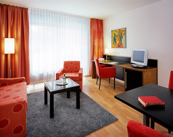 Une chambre d’hôtel avec un canapé, une table à manger, un bureau avec un ordinateur, une chaise et un tableau au mur.
