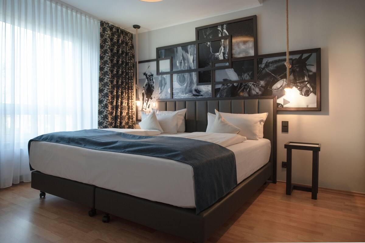 Une chambre moderne avec un grand lit, une tête de lit ornée d’une œuvre d’art, une table de chevet et un luminaire suspendu.